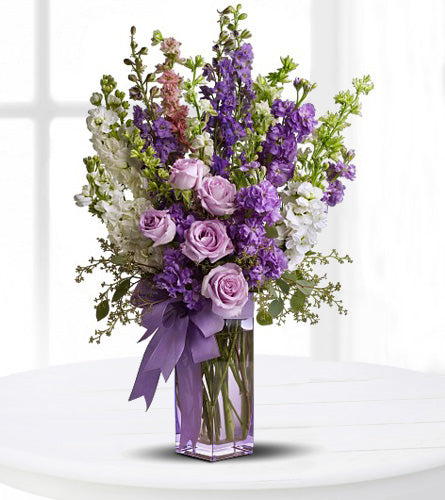 Purple Tribute - white, mauve and purple flowers arranged in a lavender glass vase, tied with bow.