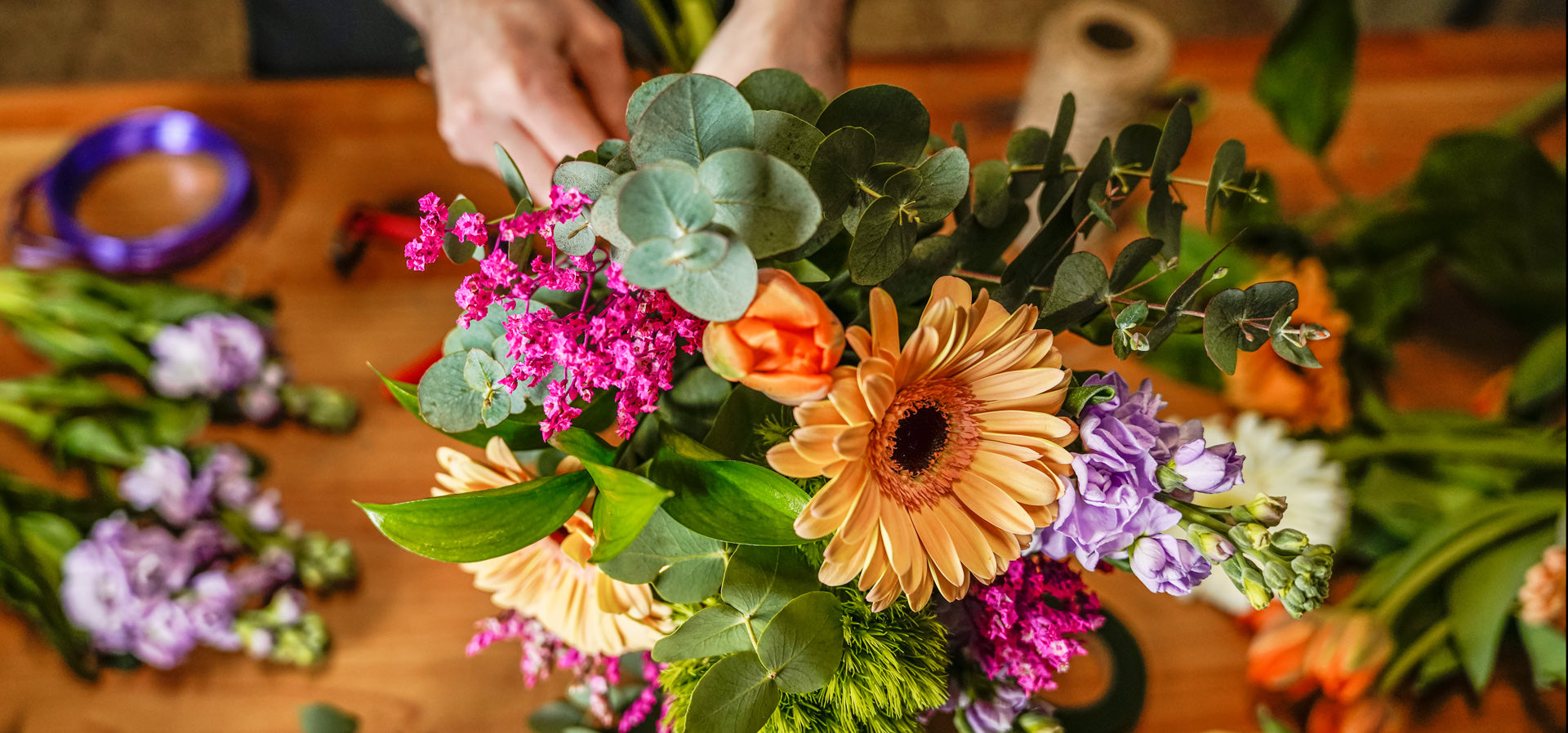 A floral designer at Nature's Wonders Florist at their workbench, making a brightly coloured bouquet of mixed flowers.